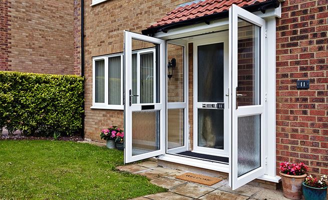 Pair of open white uPVC French doors as front doors on porch with silver letterbox and welcome mat