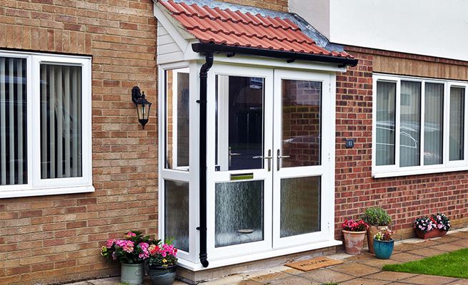 Pair of white uPVC French doors on front porch finished with obscure glass bottom and red tiled roof with black uPVC guttering