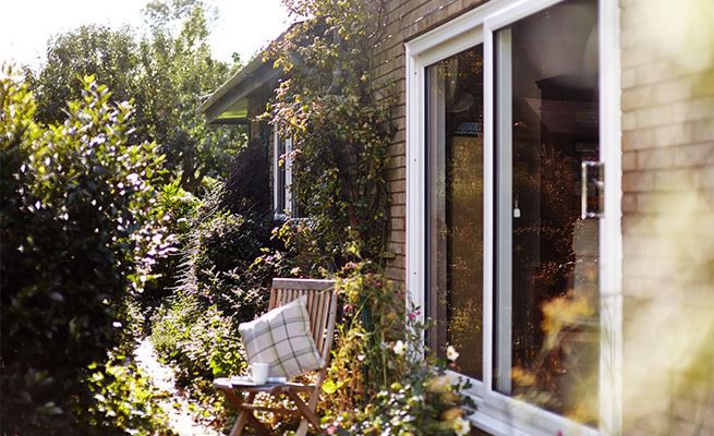 Late afternoon exterior view of white UPVC sliding doors with wooden deck chair in garden