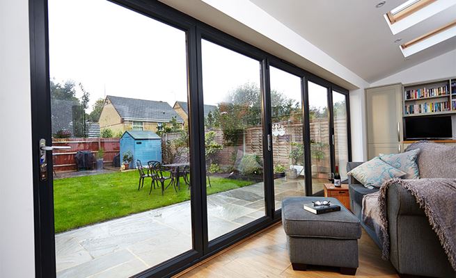 Large five panel aluminium bi-fold doors in Jet Black with chrome handles on modern living space extension