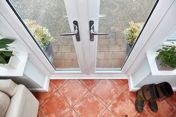 Birdseye view of pair of dual-colour cream and white uPVC French doors with chrome handles and terracotta tiled conservatory floor