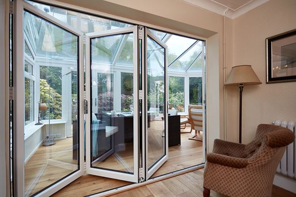 Three panel white aluminium bi-fold doors sliding open into uPVC glass conservatory dining room from the Anglian bi-fold doors range