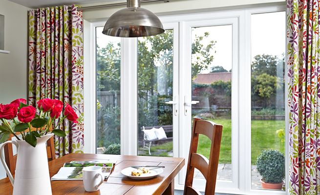 Pair of white uPVC French doors opening onto garden patio with candles and plants on the doorstep
