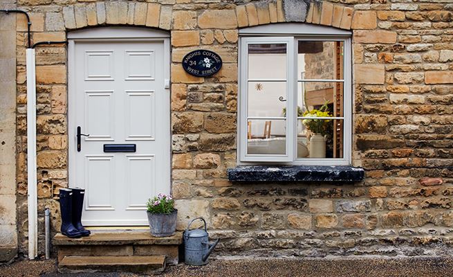 Ivory wooden Georgian style front door and matching casement windows on cottage home with stone walls