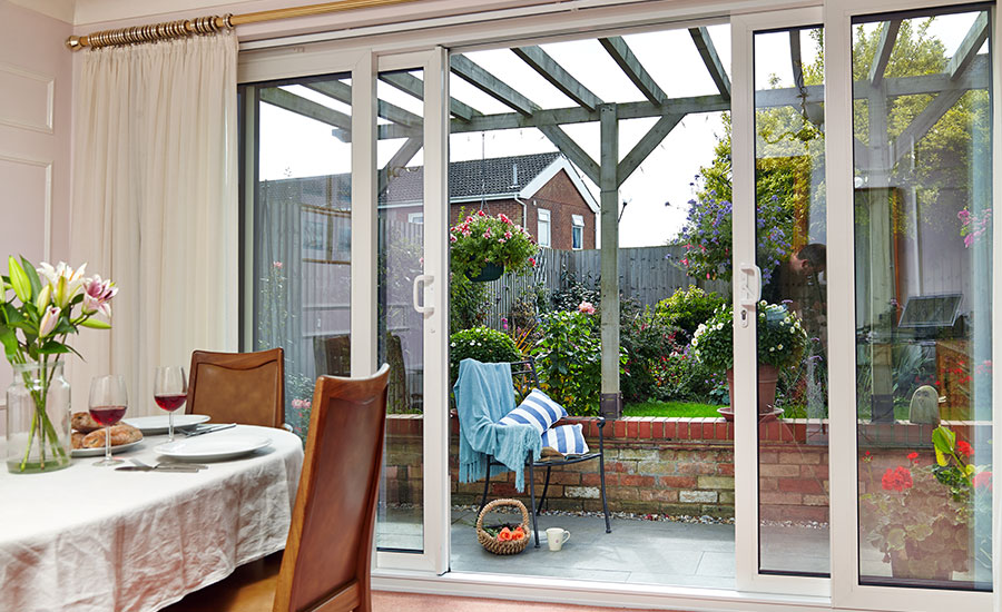 Dining room view of large white aluminium patio doors sliding open onto garden from the Anglian patio door range