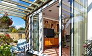 White aluminium patio doors with white handles sliding open to outside patio with timber pergola