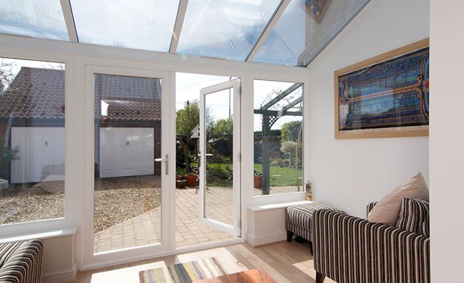 Inside UPVC lean to conservatory with French doors finished in white opening onto driveway from the Anglian conservatory range