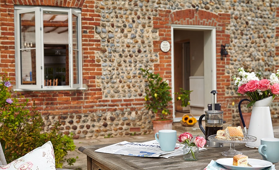 Patio view of White wooden double glazed casement window on cobblestone house from Anglian Home Improvements